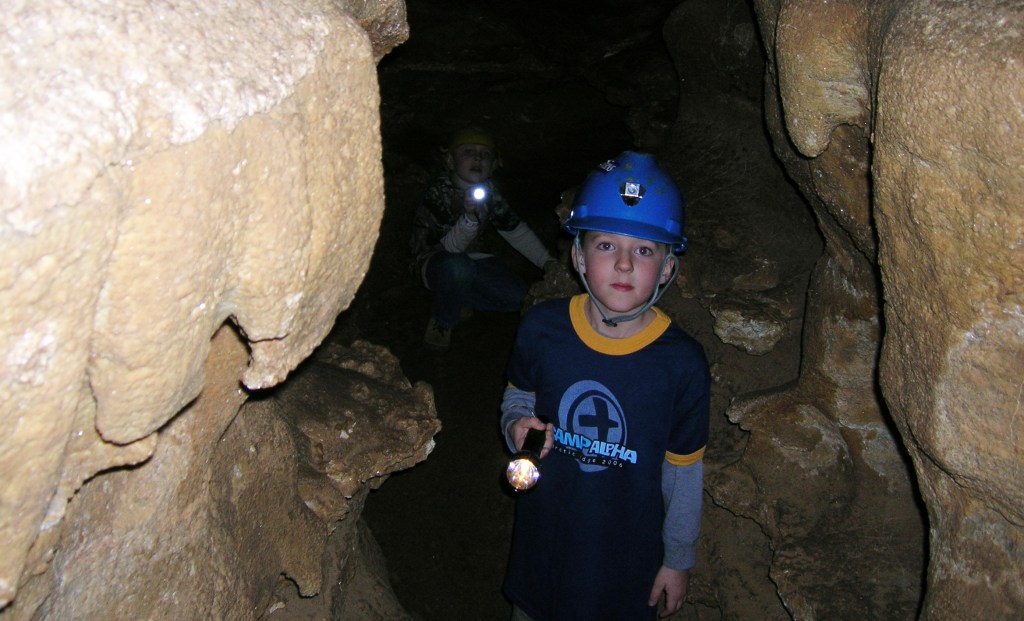 Boy with a headlamp helmet on carrying a flashlight in a cave