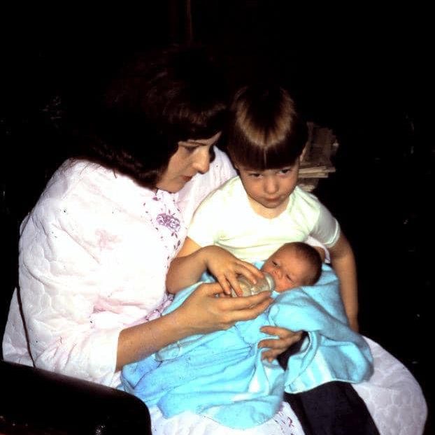 Mother holds a young boy and a baby boy on her lap
