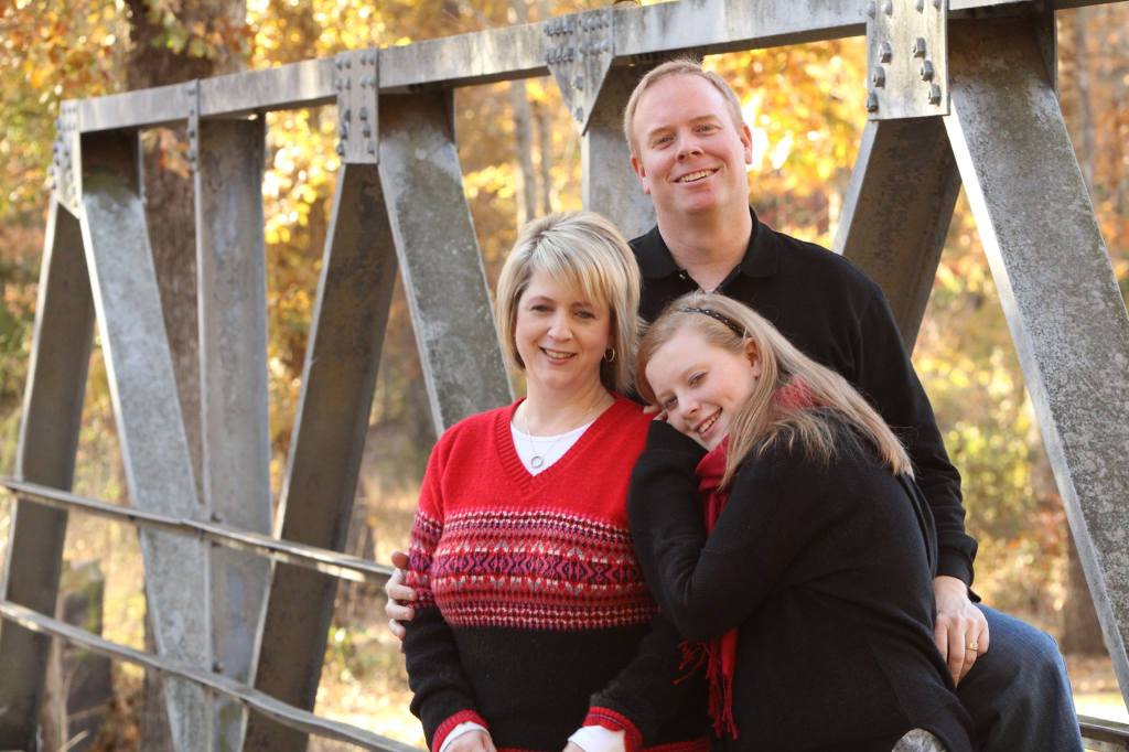 A man and his wife and their teen-aged daughter stand on a bridge during the fall.