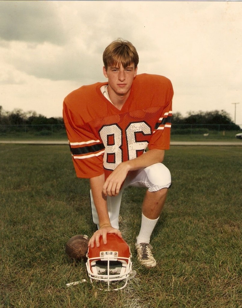 Lance Wallace in Highlander football uniform with his hand on his football helmet