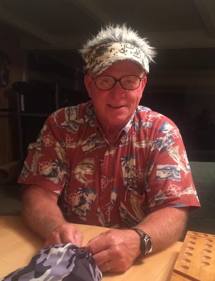 Larry Wallace in a red shirt with nautical scenes and a camo visor with built in gray and white hair standing up all over.