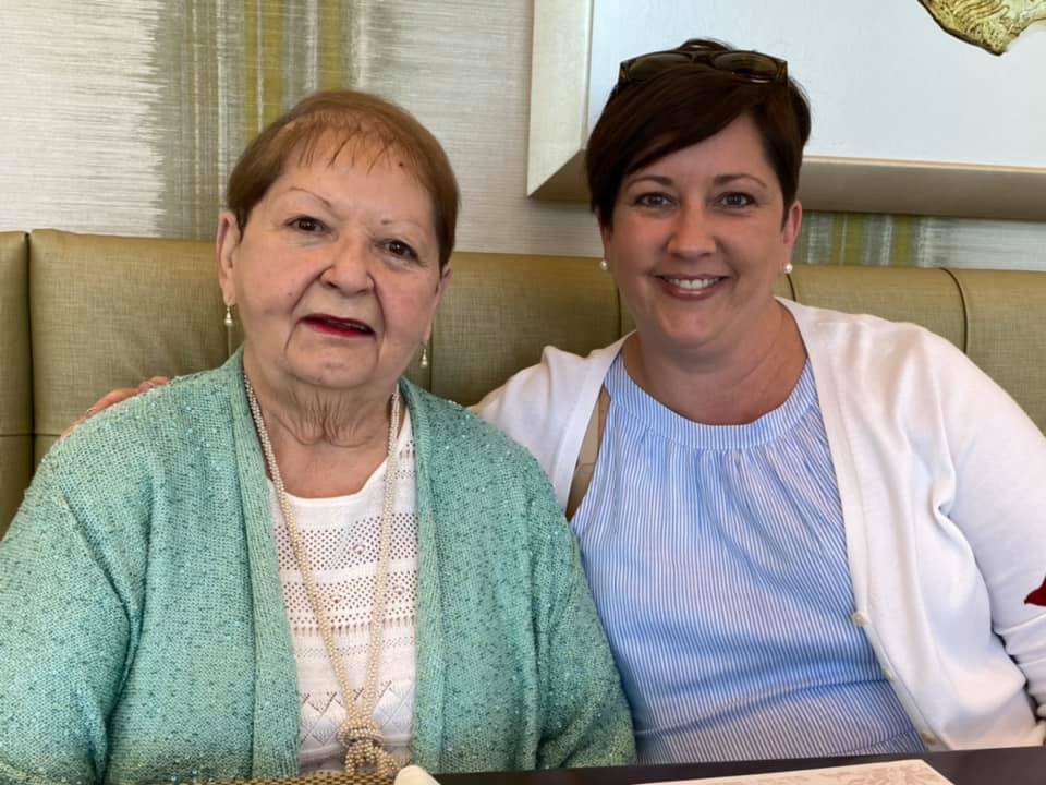 Cynthia Barron wearing a white top and green sweater sits with her daughter, Carla Wallace in a blue dress and white cardigan, at a restaurant for Mother's Day lunch.