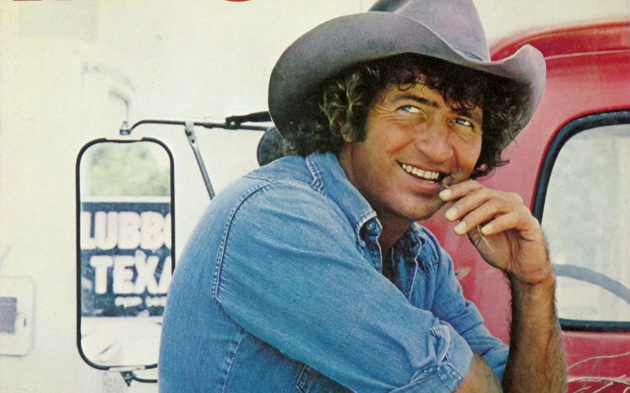 Young Mac Davis in a cowboy hat with a red pickup truck