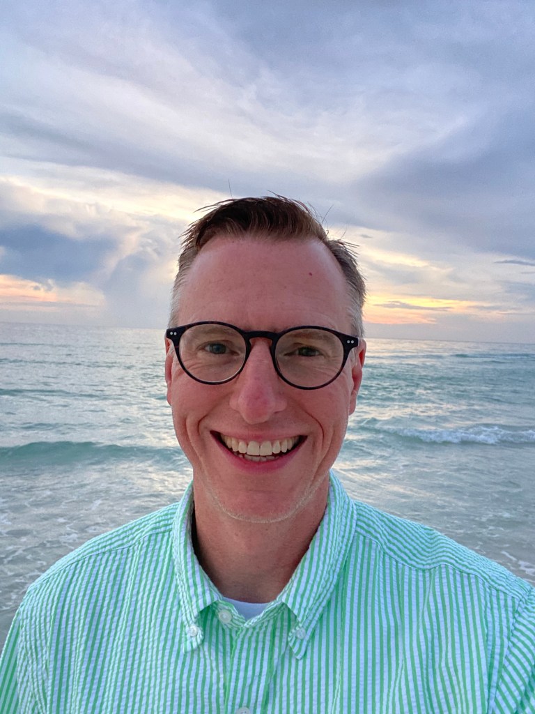 Lance Wallace in a green striped seersucker shirt on the beach at sunset