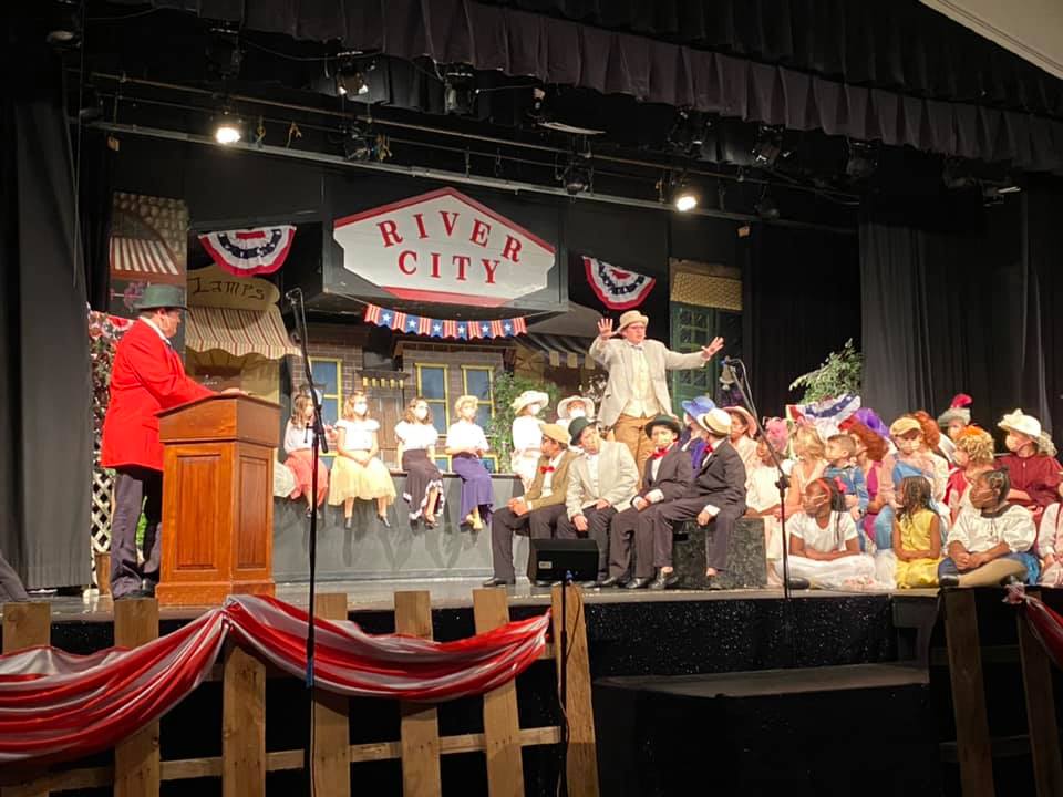 A teenager in a straw hat gets towns people’s attention on stage