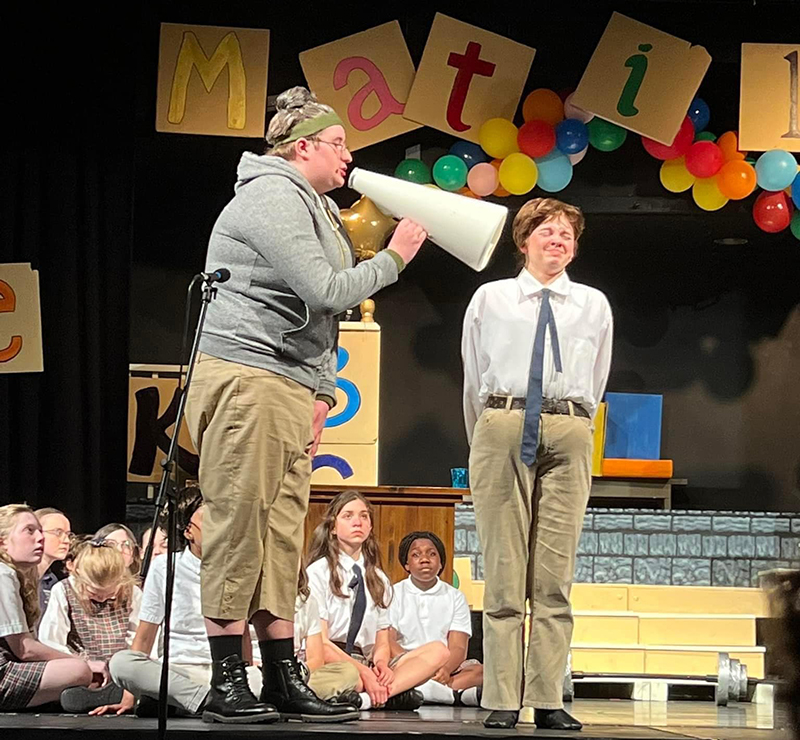 a woman in old fasioned workout clothes yells through a megaphone at a student