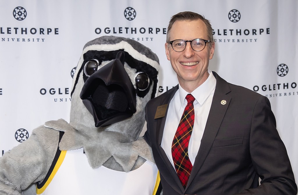 A person in a bird mascot costume and a man in a dark suit with red tie