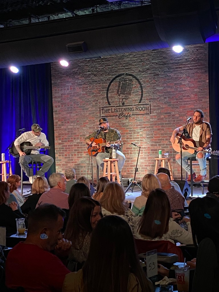 Three men on stools with acoustic guitars