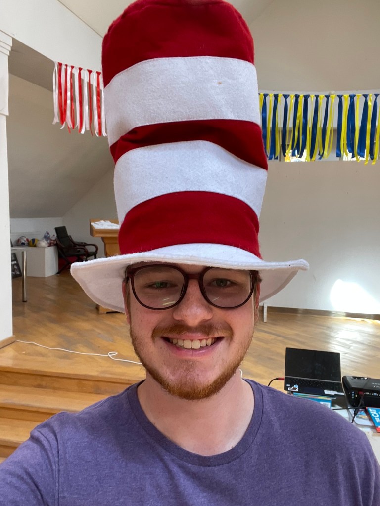 A young man in glasses and a red and white stripped elongated felt top hat