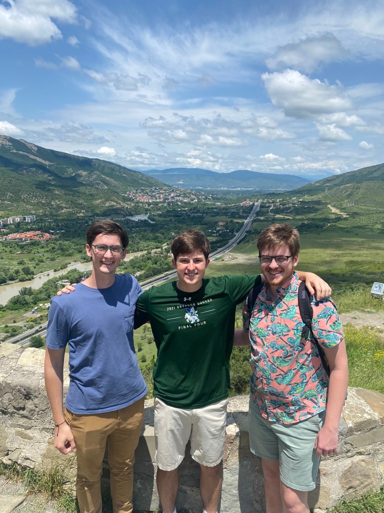 Three young man with a river valley in the backgroundd