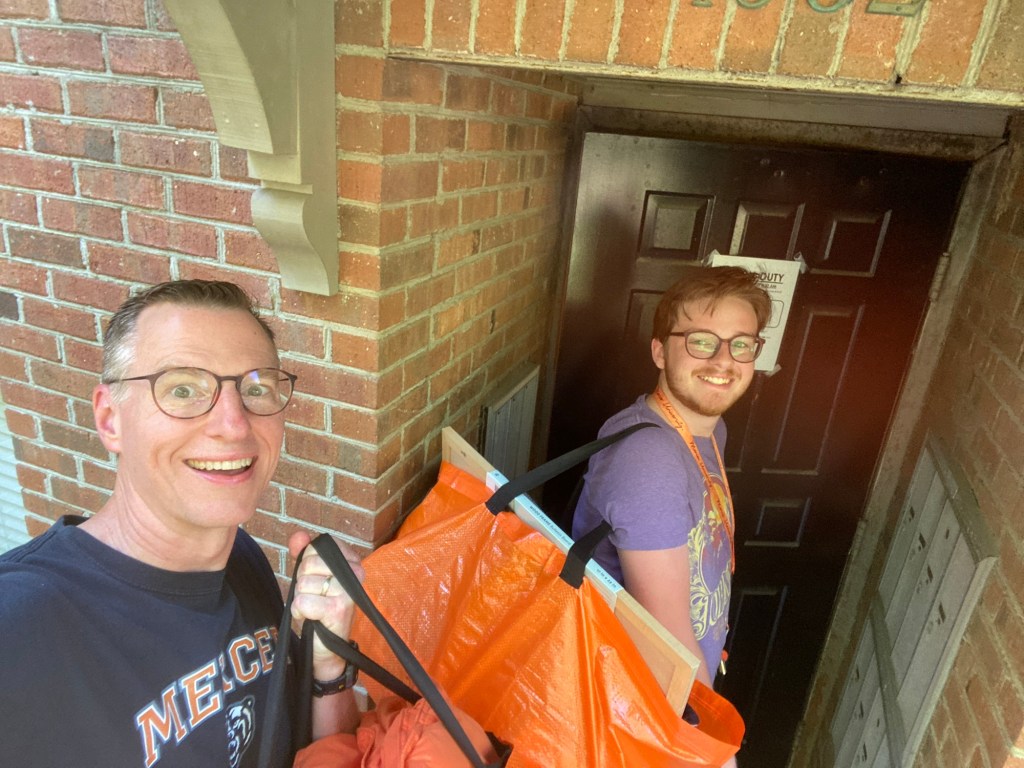 A young man and his dad carry orange bags through a door to a brick building