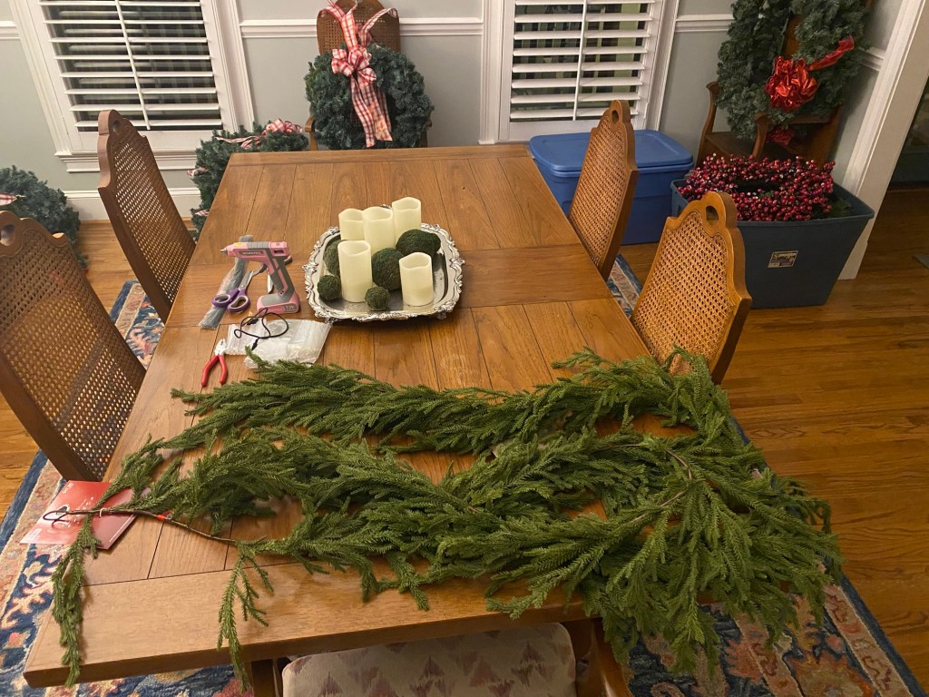 Garlands and a glue gun on a table with wreaths in the background