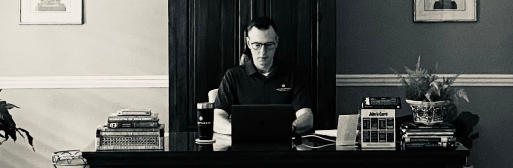 A man typing on a laptop at a desk in a home office