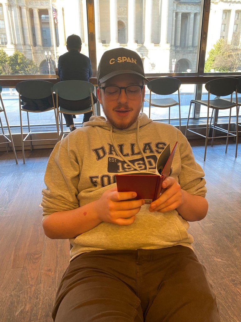 A young man reading from a small, red book