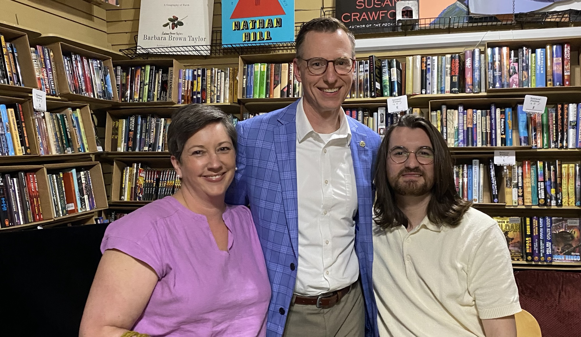 A woman and two men in front of shelves full of books