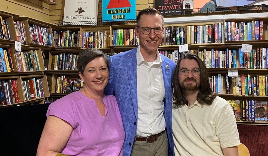 A woman and two men in front of shelves full of books