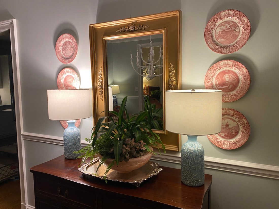 Two lamps on a buffet with a centerpiece plant in front of a wall-mounted mirror