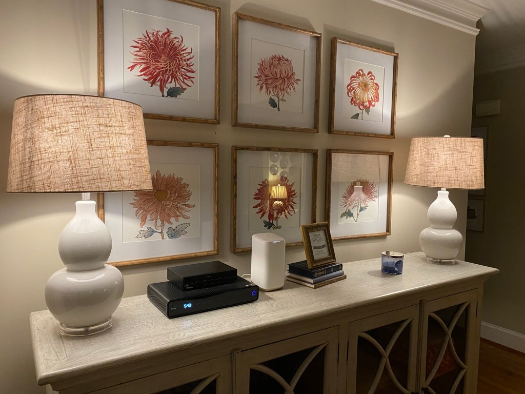 Two lamps on a bookcase under a set of six prints of flowers