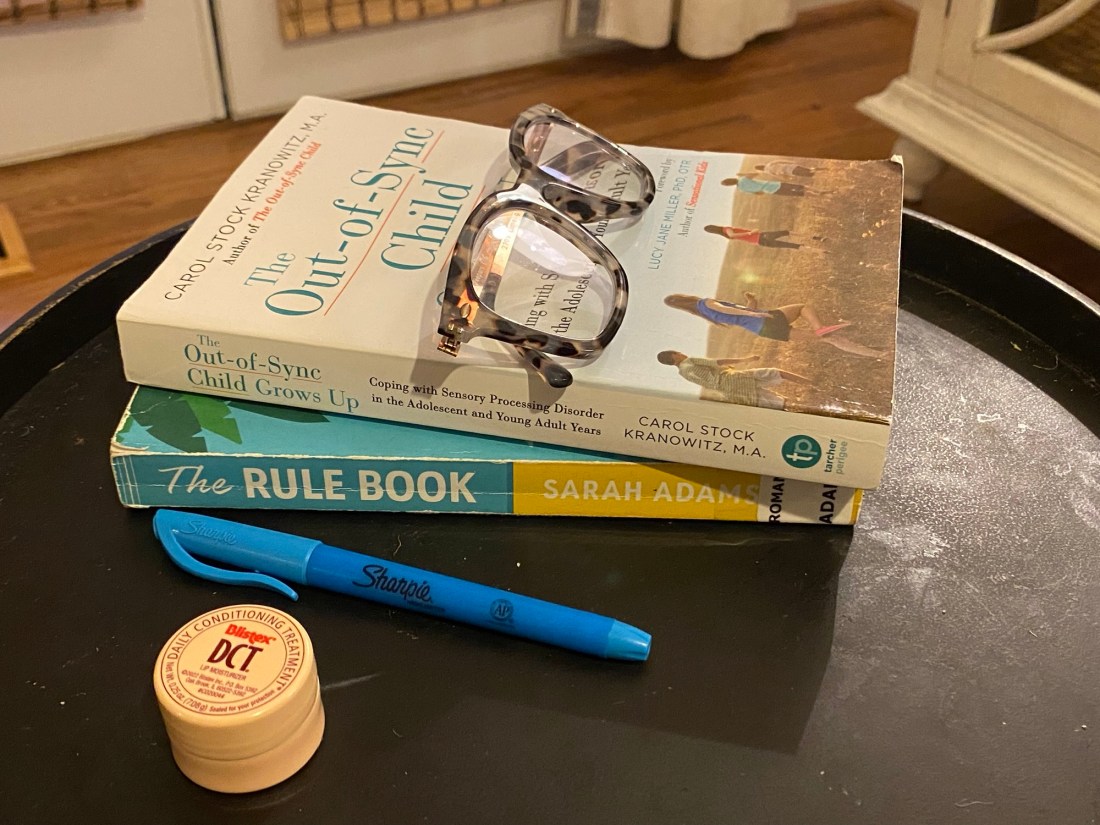 Reading glasses on a stack of books next to a highlighter and lip balm container