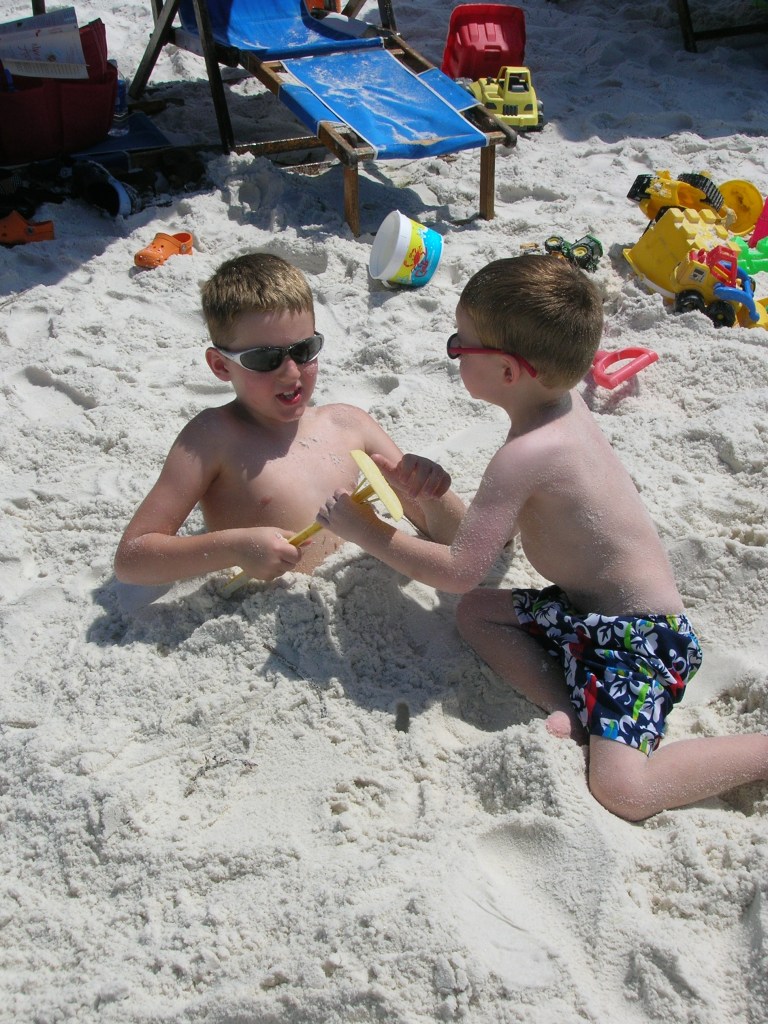 Two boys burying each other in sand at the beach