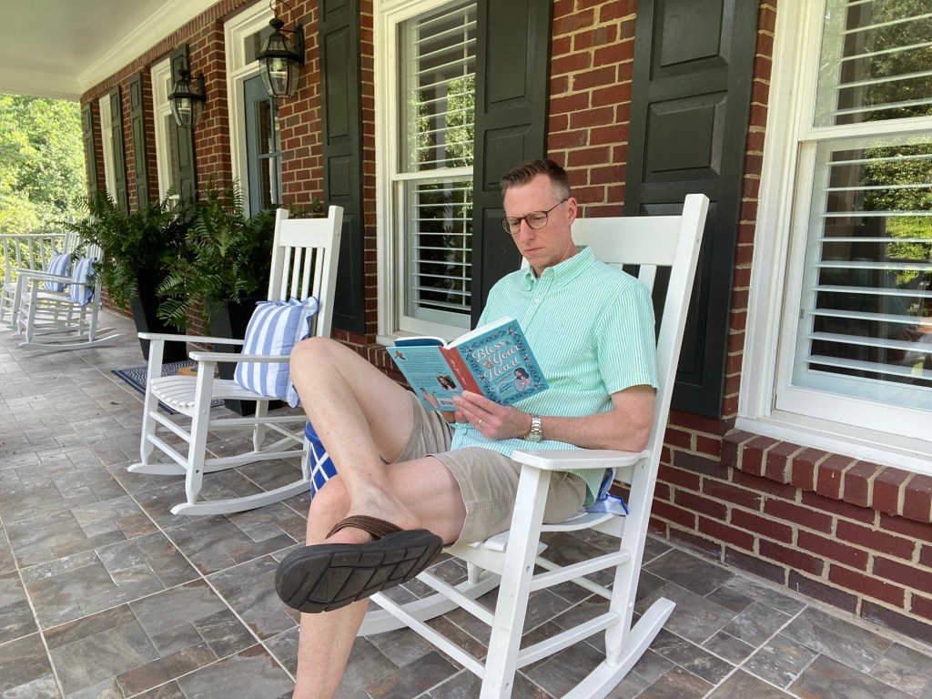 A man in a rocking chair on a porch reading a book