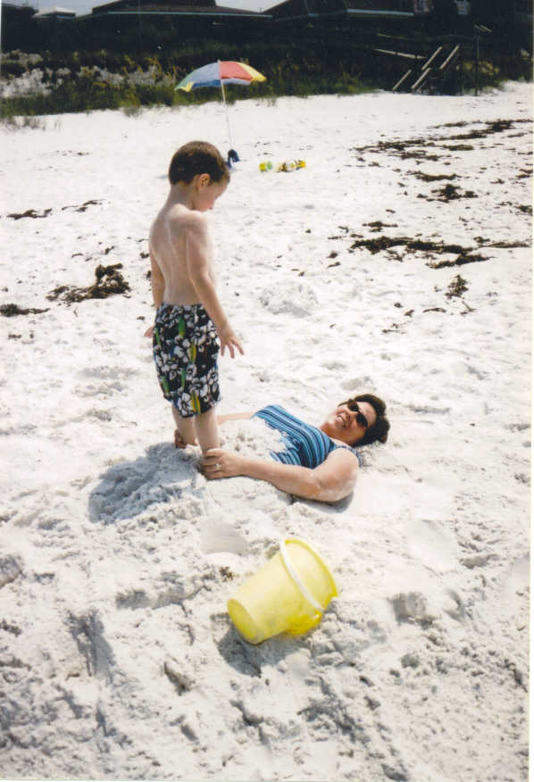 A young boy buries his mom in the sand at the beach