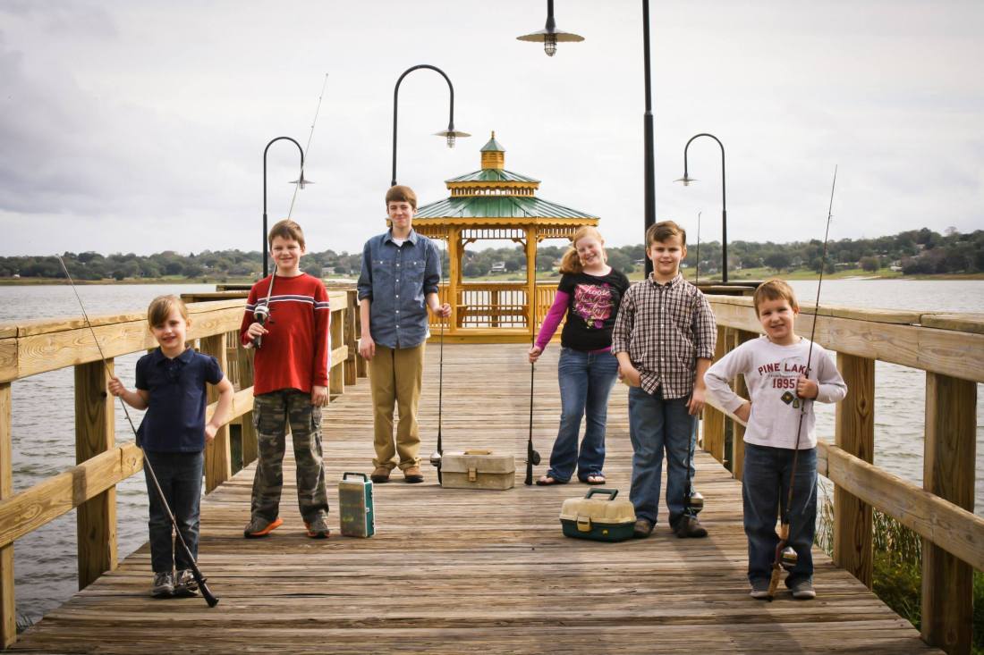 Kids lined up on a pier holding fishing poles