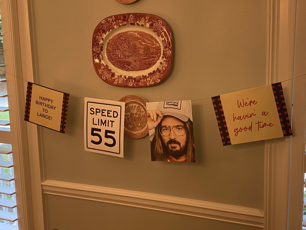 A wall decorated with a series of images strung together showing a speed limit sign, happy birthday, Dusty Slay's picture and we're having a good time.