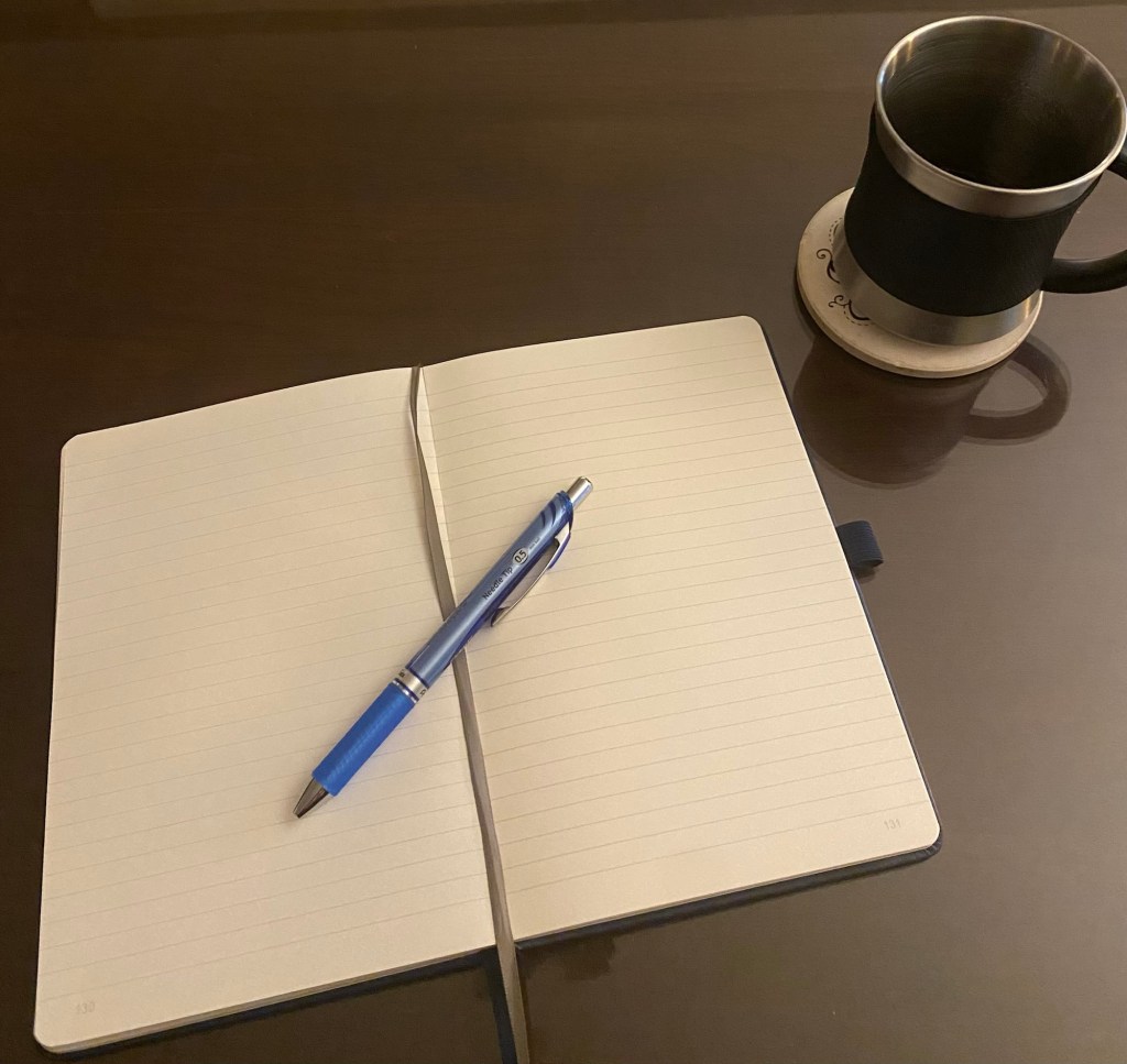 An open journal with blank pages and blue ink pen next to a cup of coffee