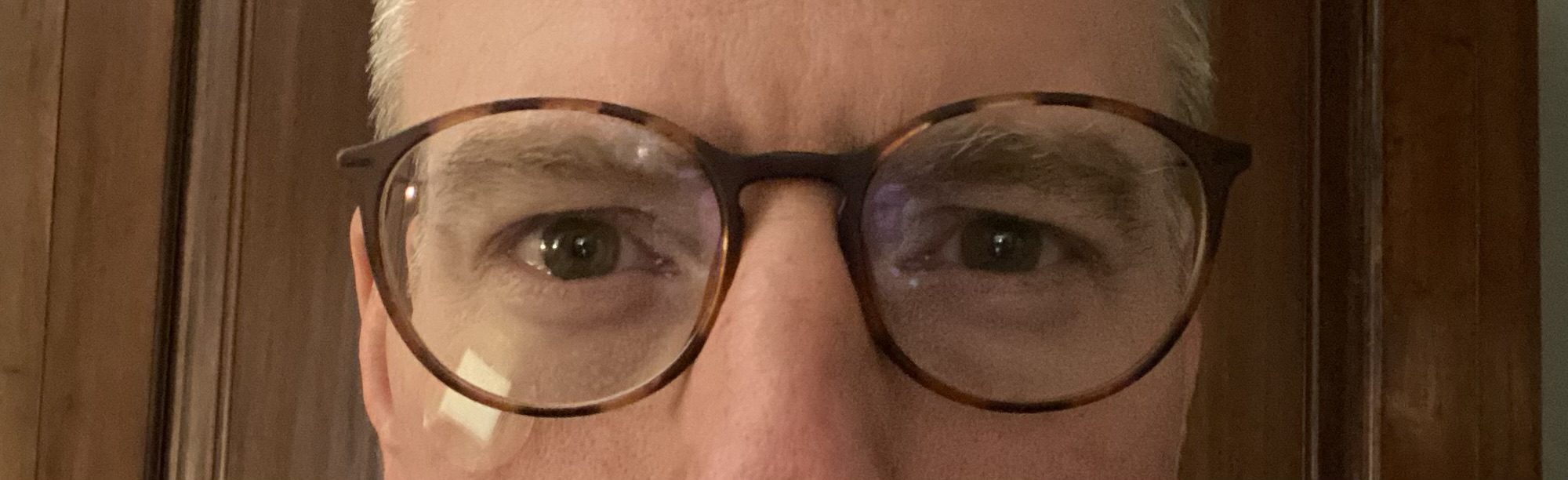 Close up of middle aged man's face with glasses and a small, round bandage under his right eye