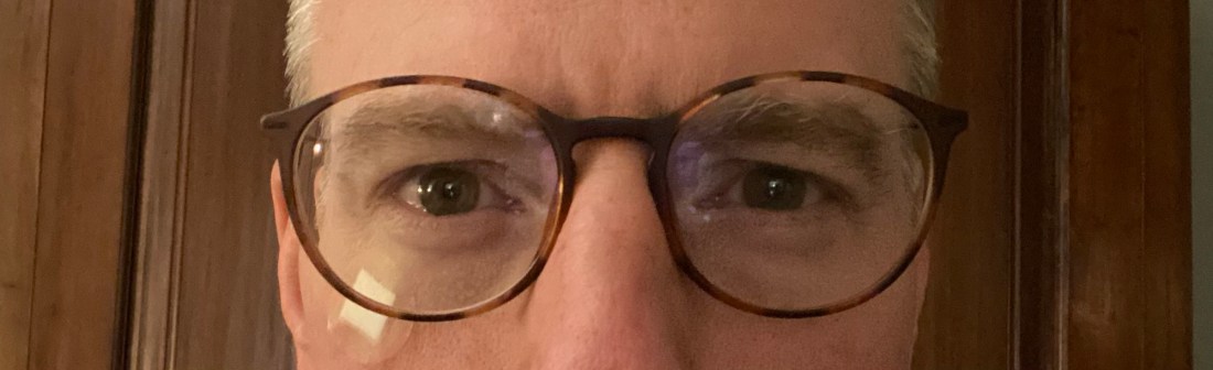 Close up of middle aged man's face with glasses and a small, round bandage under his right eye