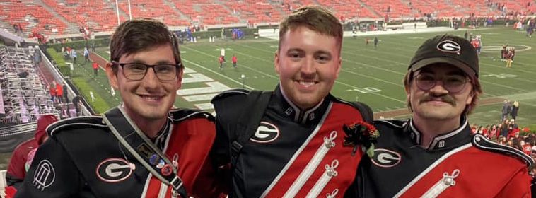 Three members of the Georgia Redcoat Marching Band arm-in-arm before a game at Sanford Stadium.