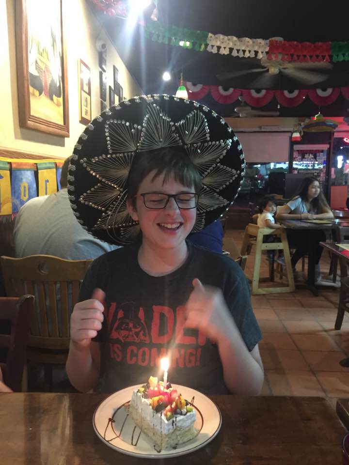 A teenager in a sombrero with a piece of tres leches cake with a lit candle in it.