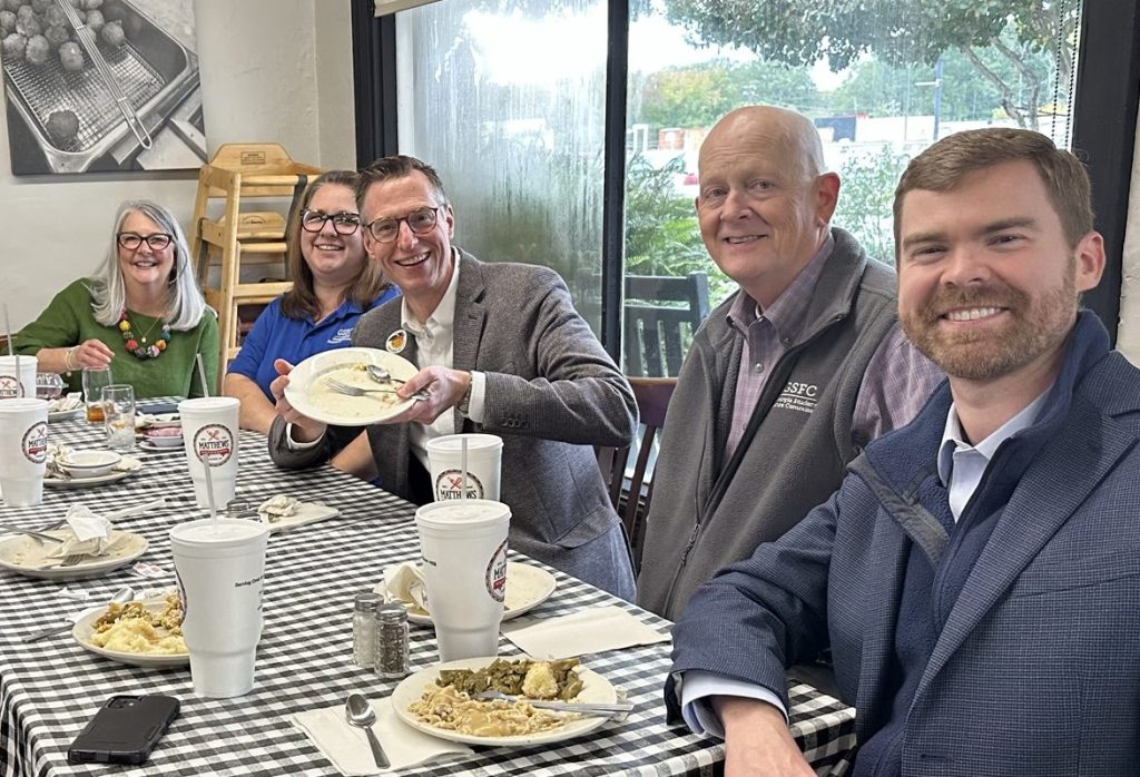 Three men and two women sitting at a lunch table with checkered tablecloths