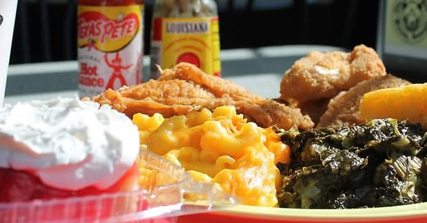 A plate of Southern food including fried chicken, macaroni and cheese, turnip greens and strawberry shortcake with Texas Pete hot sauce in the background.