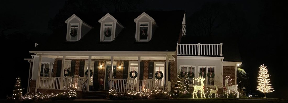 A brick house decorated for Christmas with white lights and wreaths
