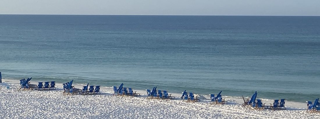 Blue waters of the Gulf of Mexico with white sand beaches in the foreground and beach umbrellas and chairs