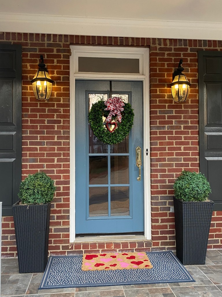 Front door with heart shaped wreath and a welcome mat covered in hearts