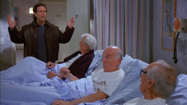 Screenshot of an episode of Seinfeld showing three old men in hospital beds with Jerry Seinfeld waving his hands and yelling at them.