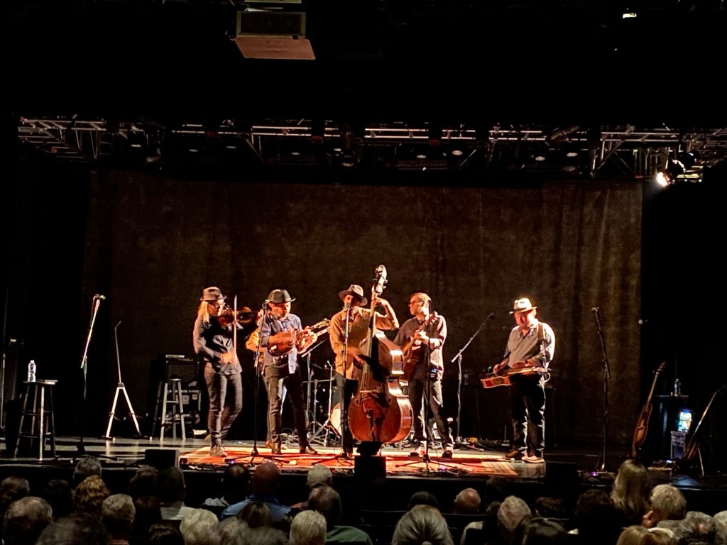 A bluegrass band performs on a stage with the audience in the foreground.