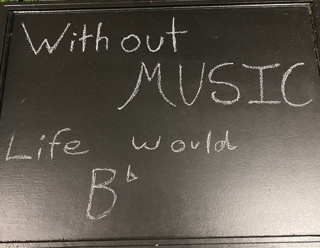 A black chalkboard with the phrase "Without Music Life would B flat" written on it in white chalk.