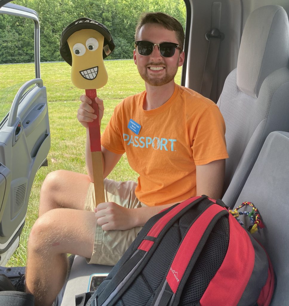 A young man holds up a yellow sponge on a stick with a wig and googly eyes.