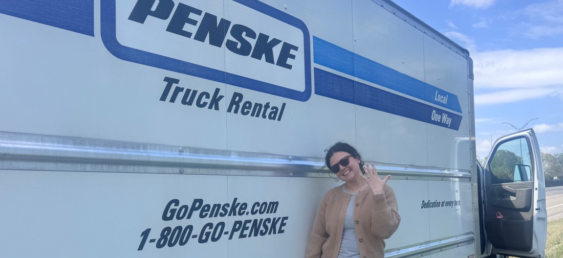 A young woman next to a Penske truck showing off her engagement ring