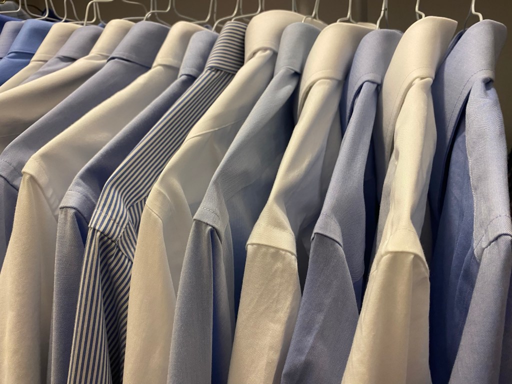 A line of alternating blue and white dress shirts on white hangers in a closet.