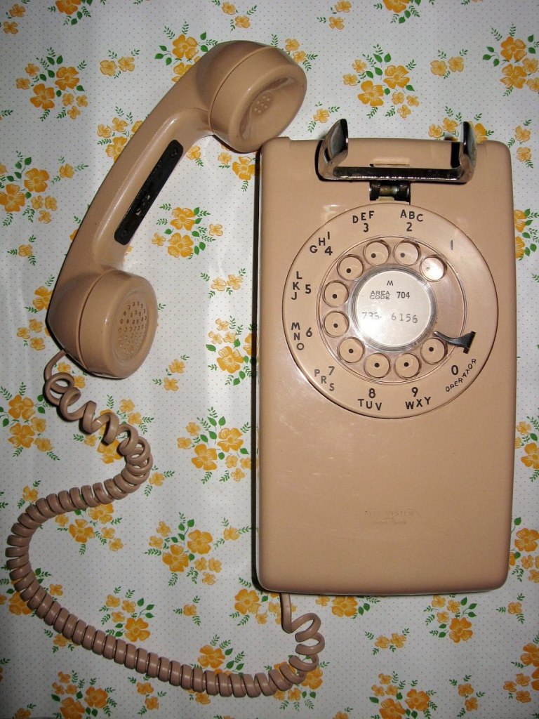 1970s beige, wall-mounted rotary telephone on flowered wallpapered wall
