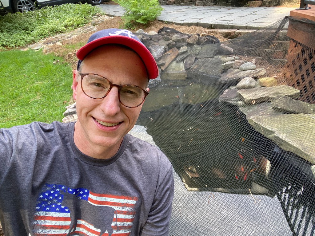 A man in a baseball cap with a goldfish pond in the background.