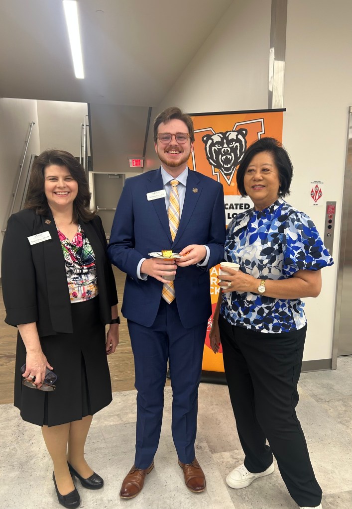 Two women stand with a young man in a suit and tie with a Mercer University banner in the background