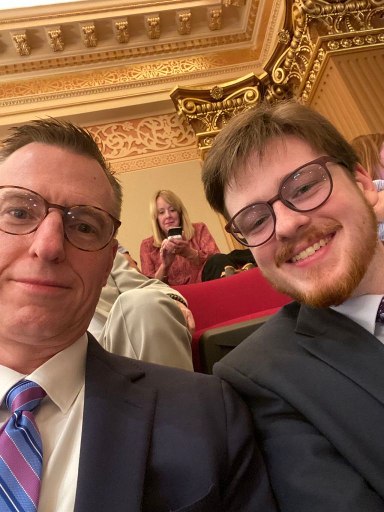 A man and his son in suits and ties in the Georgia Senate gallery.