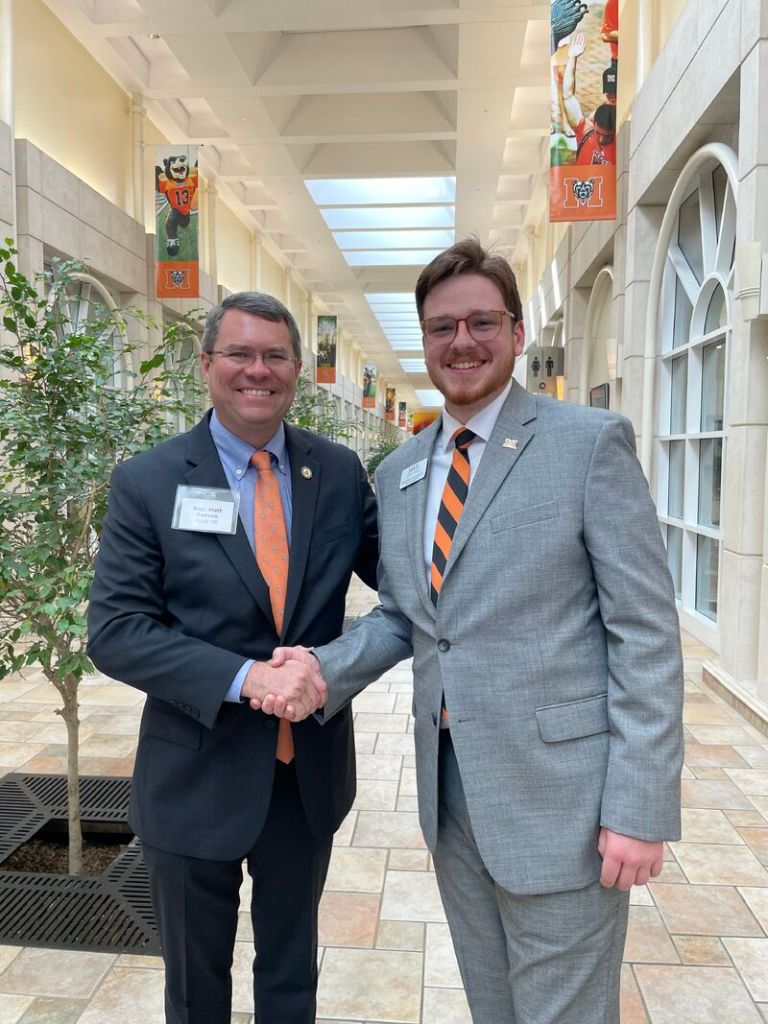 A Georgia state representative in dark suit shaking hands with a Mercer student in a light gray suit
