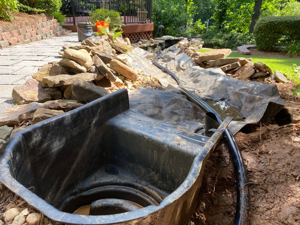 A backyard waterfall and stream with all of the rocks removes and muddy liner and basin revealed